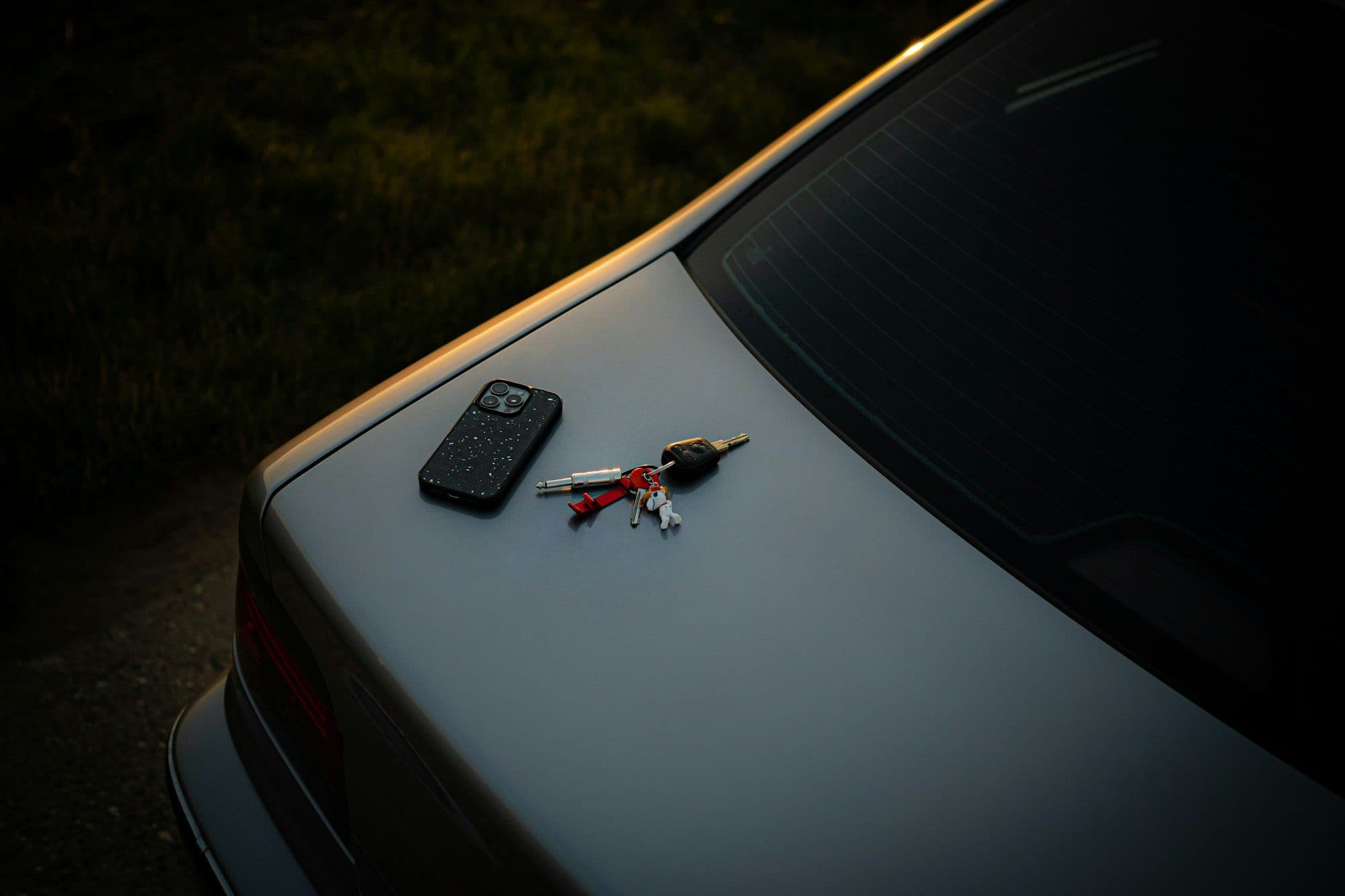 Celular e um molho de chaves sobre o porta-malas de um carro cinza ao entardecer, cena de quem vai consultar veículo pela placa