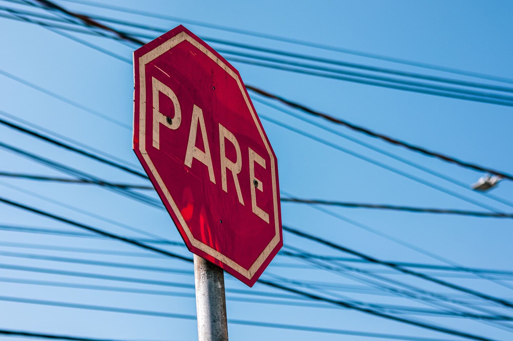 Placa de sinalização de PARE contra o céu azul, com fios elétricos ao fundo